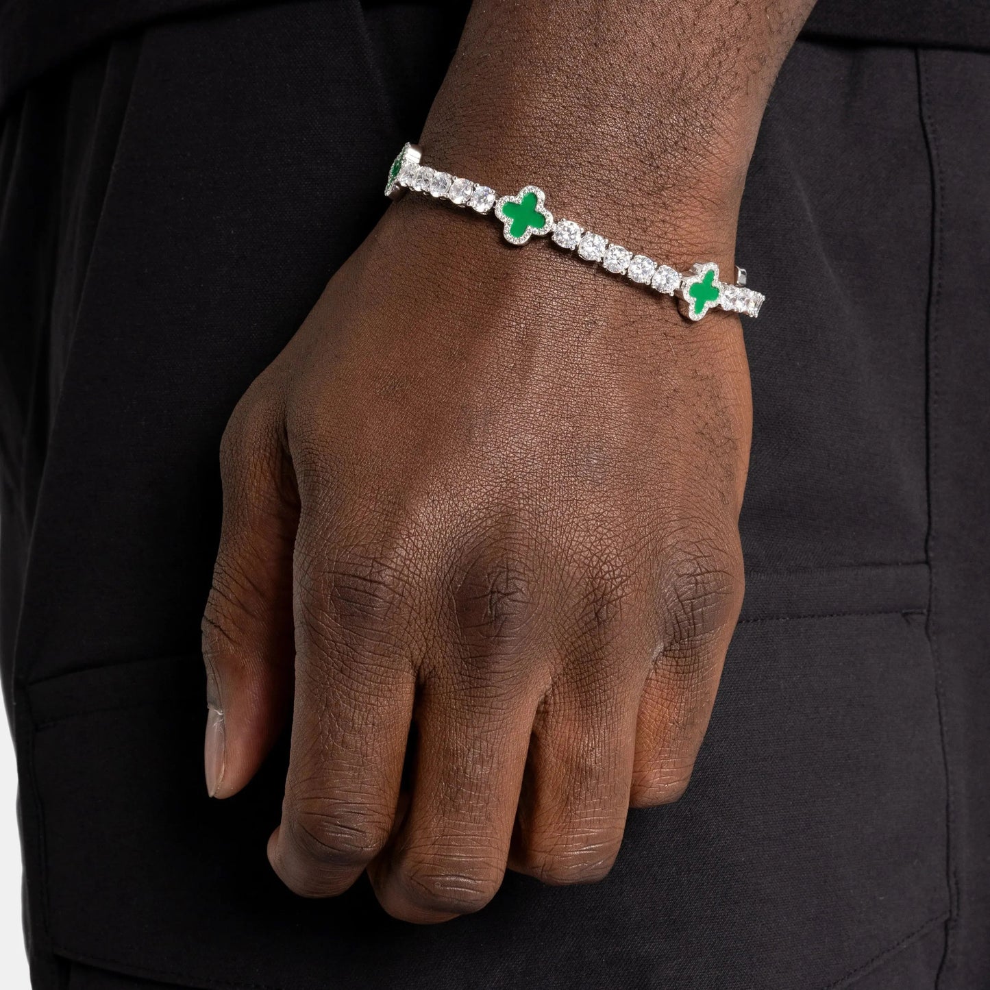 Hand wearing a bracelet with green clover charms.