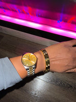 Gold watch on a wrist with A gold bracelet with diamonds  and engraved symbols.