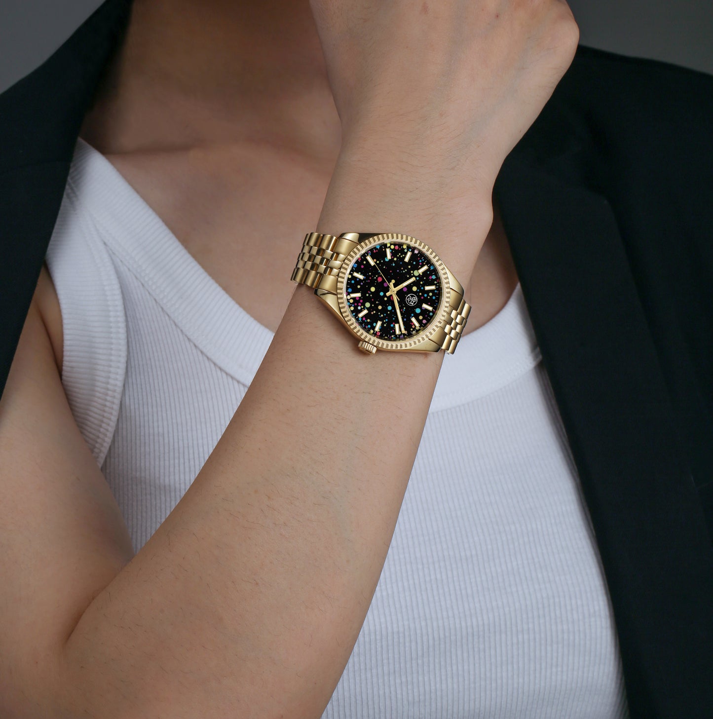 A gold watch worn by lady dressed for work,  with a multicolored dial and a classic five link bracelet with fluted bezel.
