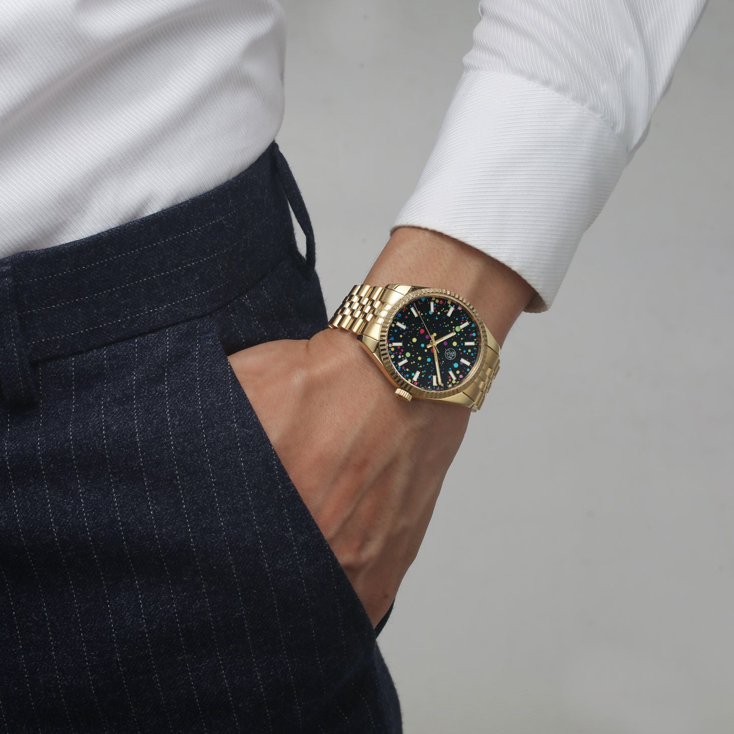A gold watch worn male finance guy dressed in white button down shirt and slacks,  with a multicolored dial and a classic five link bracelet with fluted bezel.