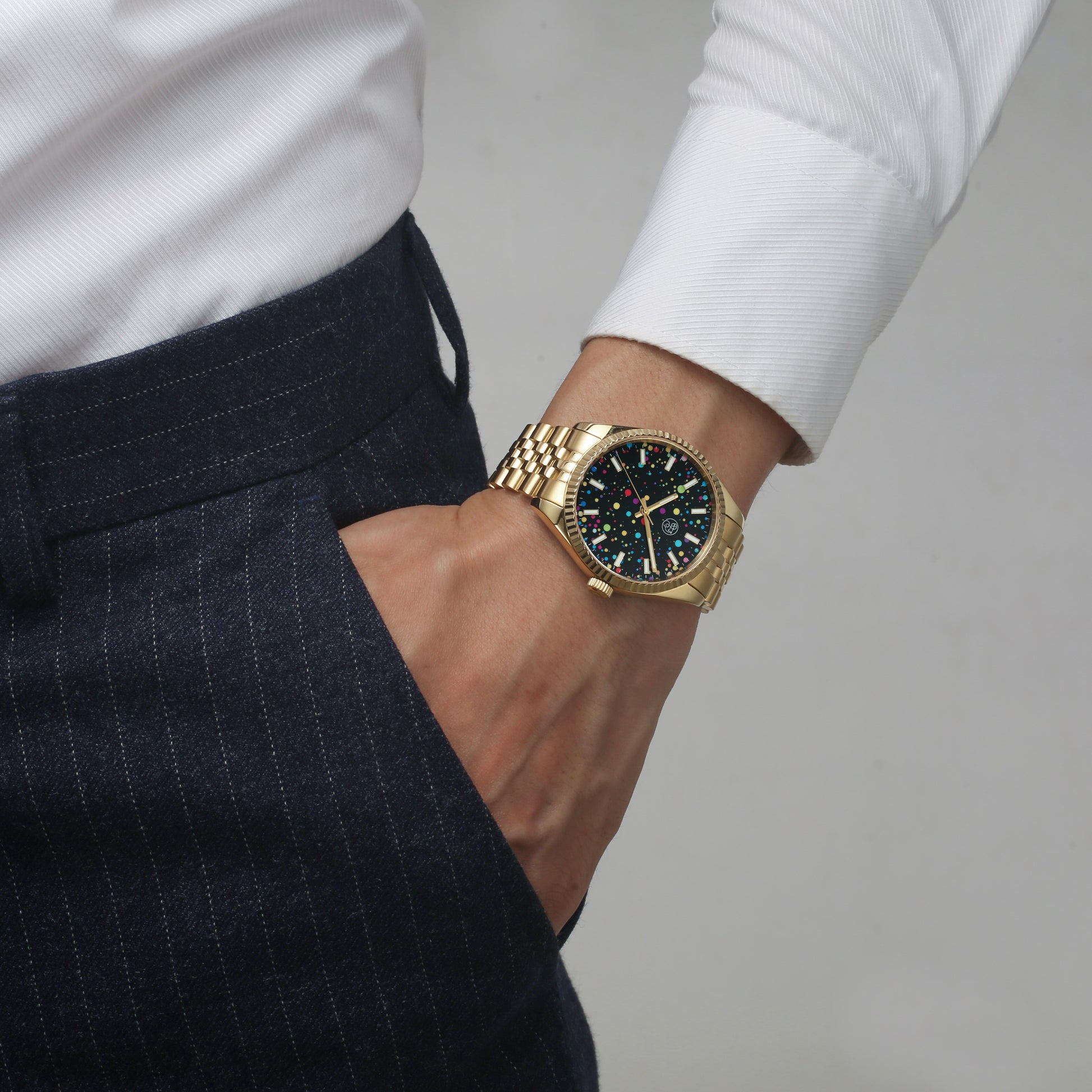 A gold watch worn male finance guy dressed in white button down shirt and slacks,  with a multicolored dial and a classic five link bracelet with fluted bezel.