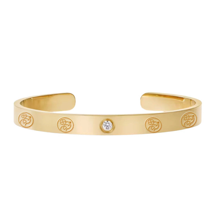 Gold bracelet with engraved symbols and a central gemstone on a white background