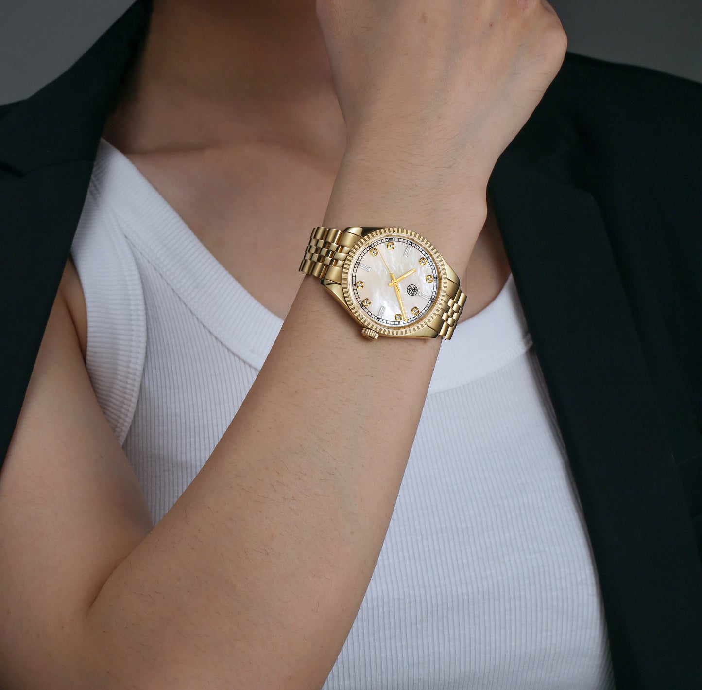 A lady wearing a gold luxury watch with a mother of pearl dial and a classic five link bracelet diamond markers 