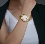 A lady wearing a gold luxury watch with a mother of pearl dial and a classic five link bracelet diamond markers 