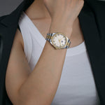 A luxury watch with a mother of pearl dial, silver and gold mixed metal bracelet, and a fluted bezel worn by a female model.