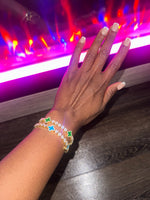 Hand wearing a bracelet with colorful clover charms against a vibrant, multicolored background.