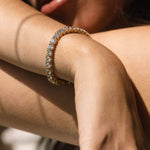 A close-up image of a person's wrist wearing a gold tennis bracelet with sparkling stones.